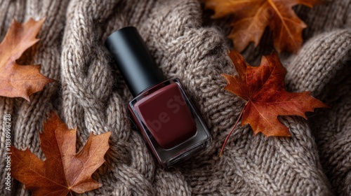 A bottle of nail polish is sitting on a blanket with autumn leaves
