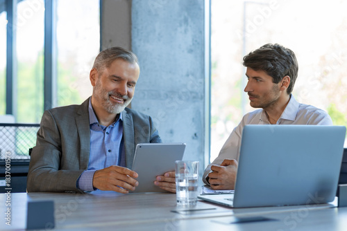 Two business people discussing work together using a tablet in a modern office