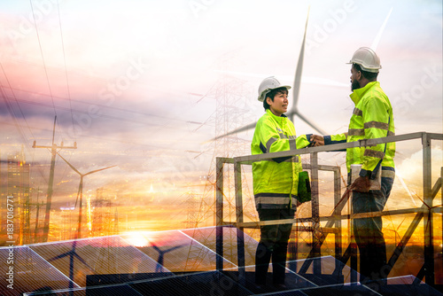 Two engineers in high-visibility vests shaking hands on an elevated platform, overseeing solar panels and wind turbines at sunset, representing partnership, renewable energy, and sustainable developme