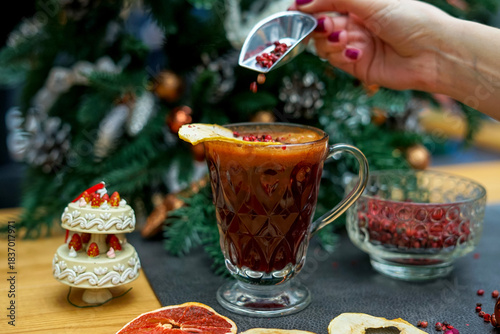 mulled wine in a transparent cup on a table with decor, a girl sprinkles spices