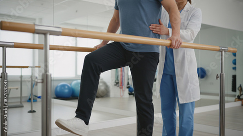 Physical therapist guiding patient taking step on parallel bars for rehabilitation and recovery