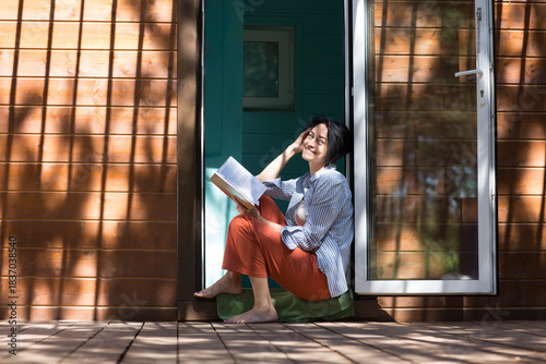 Mindfulness and feel-good moments.  lifestyle portrait smiling middle aged woman reading a book while sitting on the porch of a country house in the forest. mental health. dopamine hobbies