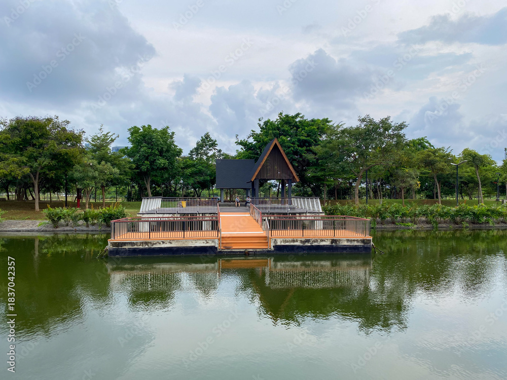 Fototapeta premium Dark wooden pavilion with a stepped roof on a floating wooden platform over calm water in PIK 2 recreation park.