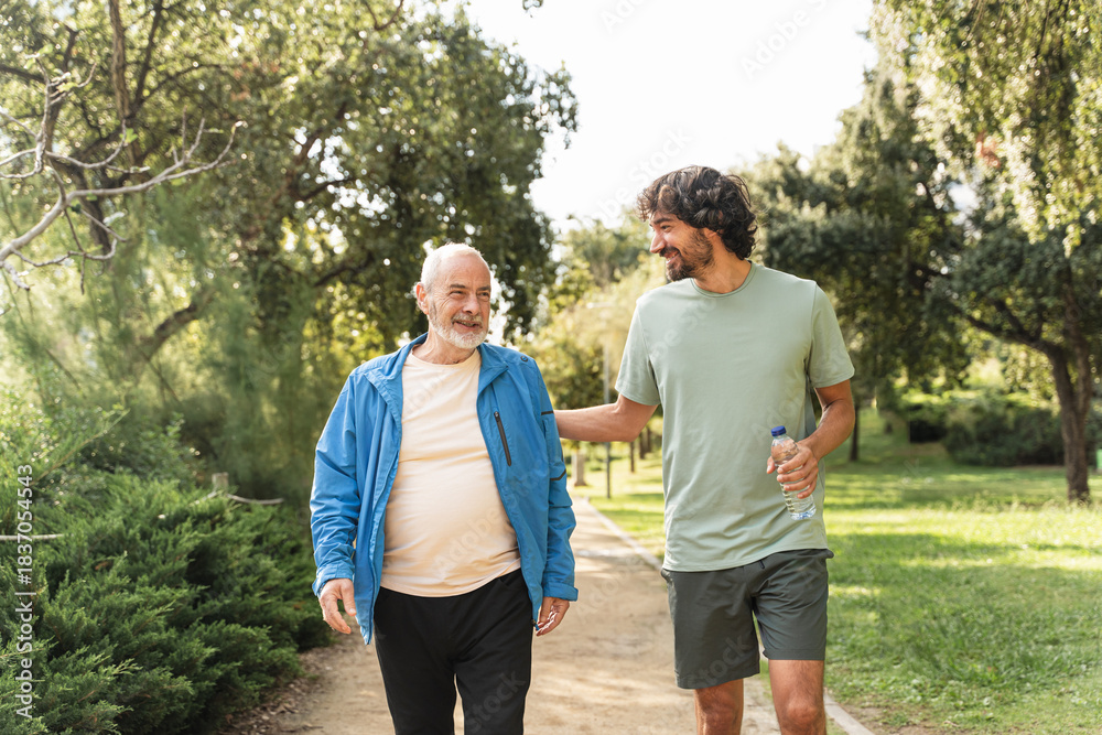 Obraz premium Smiling senior man jogging in the park together with young son, talking and supporting each other 