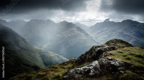 An overcast day hangs over the rugged mountain range, as light streams through the clouds onto the green slopes of the Scottish Highlands vista landscape.