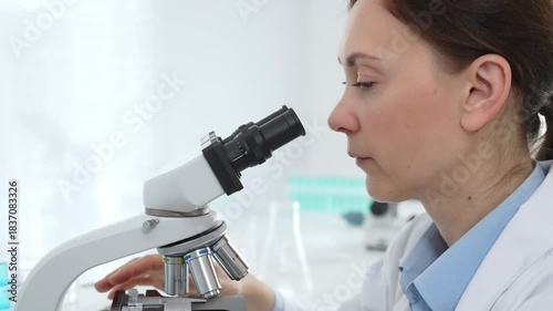 Female scientist examining samples through a microscope in a modern lab, conducting pharmaceutical research and developing treatments. Medicine, healthcare and science concept