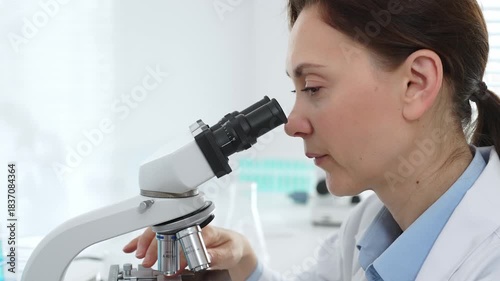 Female scientist examining samples through a microscope in a modern lab, conducting pharmaceutical research and developing treatments. Medicine, healthcare and science concept