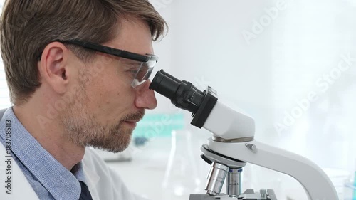 Male scientist wearing white lab coat and glasses is using a microscope is doing scientific research in a modern laboratory. Medicine, healthcare and science concept