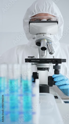 Scientific researcher wearing protective gear adjusting microscope, analyzing lab samples with precision in sterile research environment. Medicine, healthcare and science concept