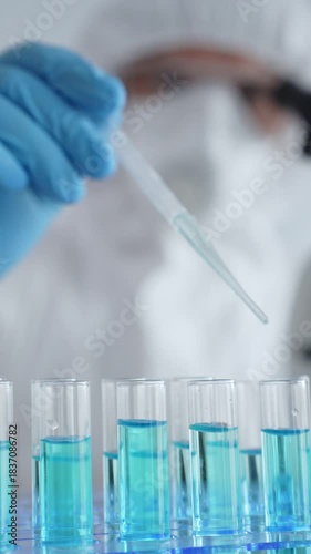 Scientific researcher wearing protective equipment, carefully pipetting liquid into test tubes while conducting medical research experiment. Medicine, healthcare and science concept