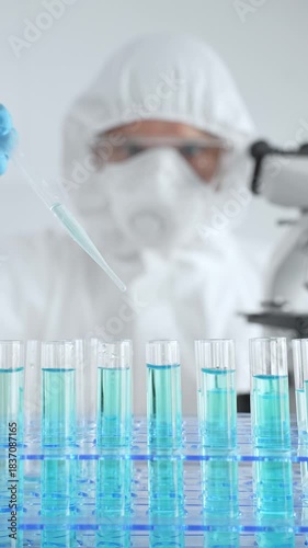 Scientific researcher wearing protective equipment, carefully pipetting liquid into test tubes while conducting medical research experiment. Medicine, healthcare and science concept