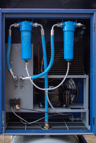 Industrial compressed air dryer cabinet, highlighting two bright blue filtration canisters connected by steel tubing and high-pressure hoses for moisture and impurity removal