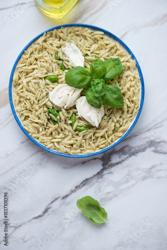 Plate of orzo pasta with torn mozzarella and basil oil on a white grenite background, vertical shot with space, flat lay
