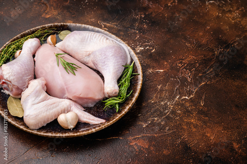 Tableau sur toile The promise of a perfect roast: prime raw poultry cuts rest with fragrant rosemary, thyme, and garlic on a deep, earthen plate, awaiting their culinary transformation