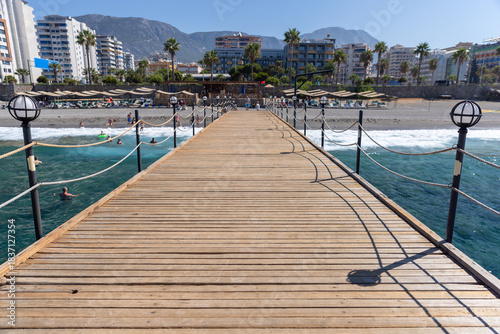 Fototapeta Naklejka Na Ścianę i Meble -  A wooden pier extends into clear blue water, bordered by a sandy beach