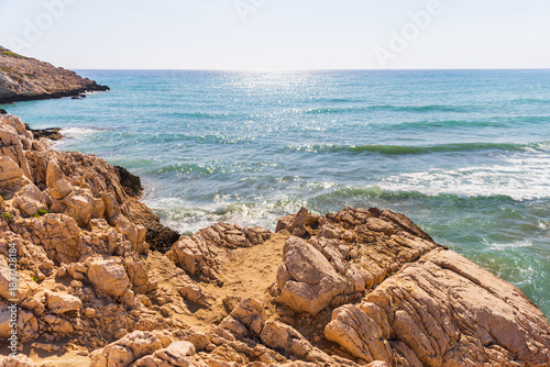 Fototapeta Naklejka Na Ścianę i Meble -  Rugged rocky coastline meets clear turquoise water under a bright sky. Craggy cliffs