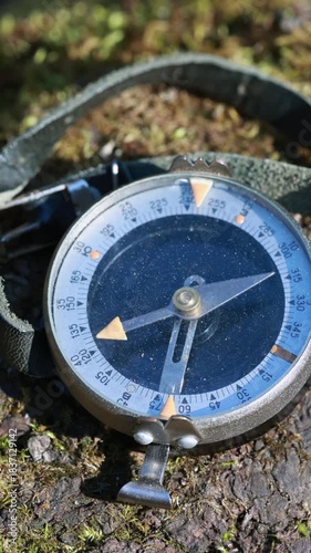 Close Up Of An Old Compass Lying On Mossy Ground. Its Magnetic Pointer Quivers And Moves Unpredictably, Indicating Possible Interference Or Instability. Vertical