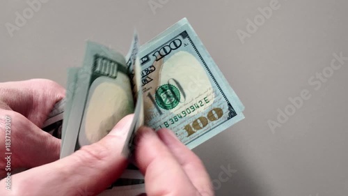 Close-up of hands counting a stack of hundred dollar bills against a light background