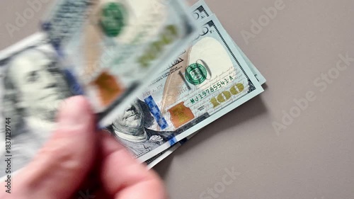 Close-up of a man's hand placing hundred dollar bills on a table
