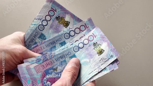 Close-up of hands counting a stack of ten thousand Kazakhstani tenge banknotes with an image of a snow leopard