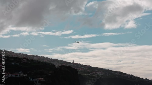Airplane gracefully glides over coastal landscape, showcasing dramatic clouds and hillside, with a smooth camera pan capturing the scene's beauty