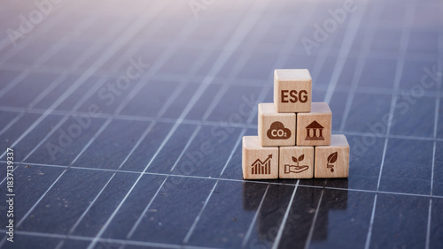 ESG wooden cubes stacked in pyramid on solar panel with finance and nature icons.