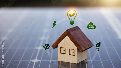 Wooden house model on solar panel with energy saving light bulb and eco icons.
