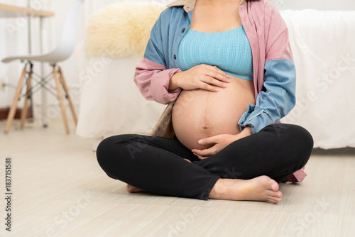 A pregnant woman sits cross-legged in a cozy room, gently forming a heart shape over her belly. The scene captures maternal anticipation, emotional connection, and the warmth of prenatal love