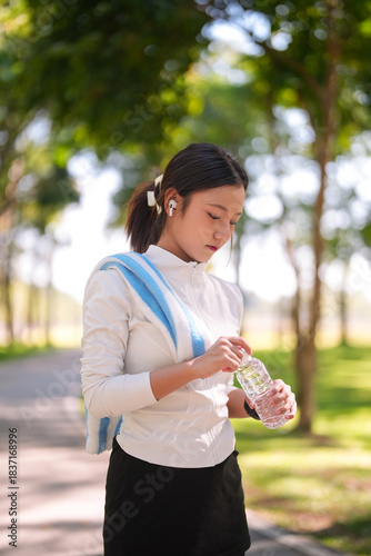 Asian young adult woman rehydrates outdoors after exercise workout at park maintaining active lifestyle and wellness