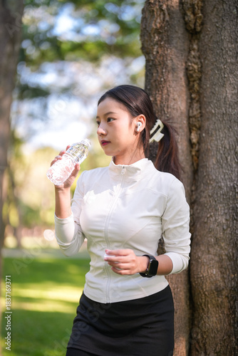 Wallpaper Mural Asian woman drinking water bottle outdoor park maintaining healthy lifestyle fitness training session refreshment hydration Torontodigital.ca