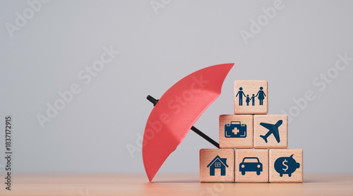 Wooden blocks with icons for family health travel home car and savings under an umbrella symbolizing financial protection and risk coverage as an mortgage asset insurance concept
