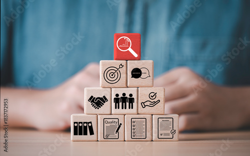 A quality audit concept using wooden blocks arranged in a pyramid illustrating compliance performance review documentation teamwork and business process improvement for effective corporate management.