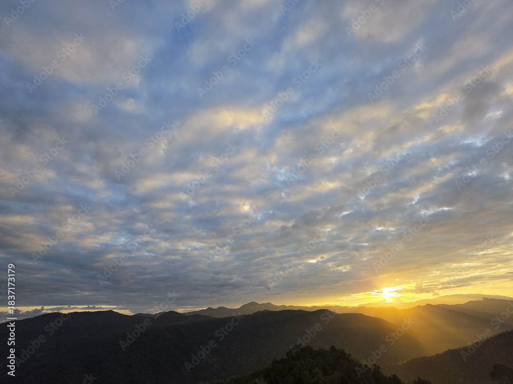Fototapeta premium Beautiful sunrise over mountain range. tranquil golden light from sun illuminates scenic sky filled with clouds. peaceful morning nature landscape with sun rays