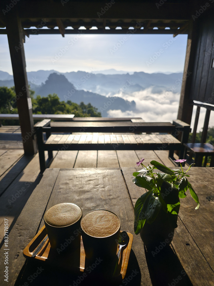 Obraz premium Tranquil morning coffee for two on wooden table with peaceful, relaxing, romantic view of mountain and sea of fog from beautiful cafe balcony viewpoint