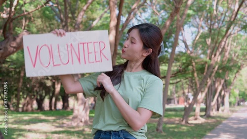 Young Volunteer: A dedicated woman holds up a sign, inviting others to join her in making a positive change. Surrounded by nature, she embodies the spirit of selflessness and community.