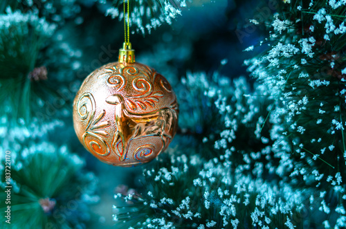 A stunning copper-gold Christmas bauble featuring an embossed reindeer design hanging on a frosted pine tree. This elegant ornament adds a classic touch to the festive holiday decor.