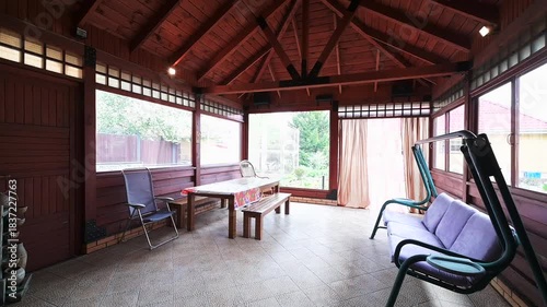 Spacious covered patio with exposed wooden beams, brick walls, and tiled floor. Features a dining table, chairs, and an outdoor kitchen for relaxation
