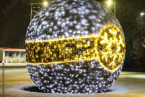 Large snow covered Christmas ornament glowing with festive lights