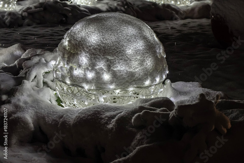 Illuminated Christmas ball covered with snow in winter night