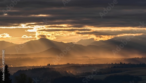 A breathtaking sunrise over the mountains, with golden sun rays piercing through the cloudy morning sky. The dramatic landscape captures the beauty of nature, peaceful atmosphere, and warm light.