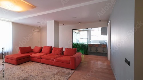 Modern open-concept living room with large orange sectional sofa, wooden flooring, recessed lighting, and green plant accents, creating a warm and inviting atmosphere.