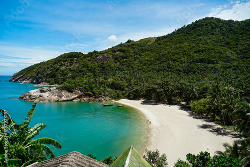 View on the Than Sadet beach,koh Phangan island,Thailand. Tropical beach shore in Koh Phangan with huge rocks, coconut palm tree, lush green vegetation and small steps leading to tourist bungalows.