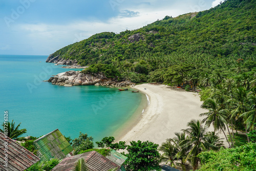 View on the Than Sadet beach,koh Phangan island,Thailand. Tropical beach shore in Koh Phangan with huge rocks, coconut palm tree, lush green vegetation and small steps leading to tourist bungalows.