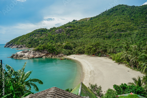 View on the Than Sadet beach,koh Phangan island,Thailand. Tropical beach shore in Koh Phangan with huge rocks, coconut palm tree, lush green vegetation and small steps leading to tourist bungalows.