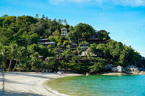 View on the Than Sadet beach,koh Phangan island,Thailand. Tropical beach shore in Koh Phangan with huge rocks, coconut palm tree, lush green vegetation and small steps leading to tourist bungalows.