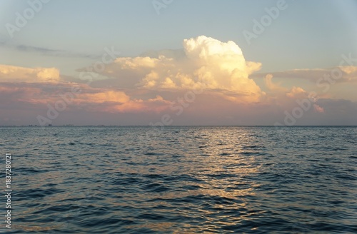 Sunlit cumulus clouds reflect over calm ocean ripples at horizon, capturing a tranquil moment of nature’s daily rhythm near Madeira Beach, Florida, U.S