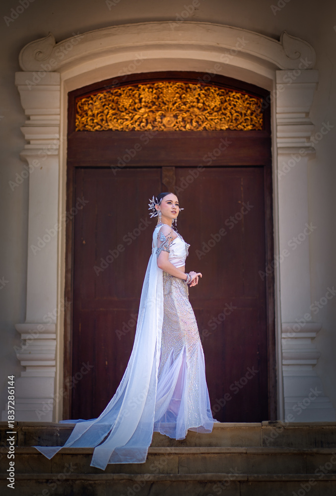 Obraz premium Graceful woman elegant white gown with long flowing train stands stone steps front of large wooden door with ornate golden decoration