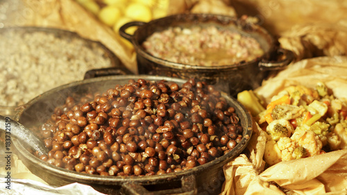 Steaming outdoor feast featuring a cast iron skillet with peas, beans, greens, and barley grains and potatoes. Cooked over an open flame. Warm, rustic even medieval communal and inviting atmosphere.