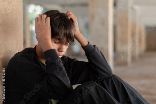 A distressed teen boy sitting on the floor with hands clutched to his head, eyes closed, symbolizing stress and anxiety.