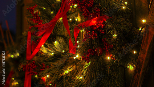 Close-up of a festive wreath adorned with red ribbons, clusters of berries, and twinkling warm lights. Creates a cozy, holiday atmosphere ideal for Christmas, home decor, and seasonal promotions.